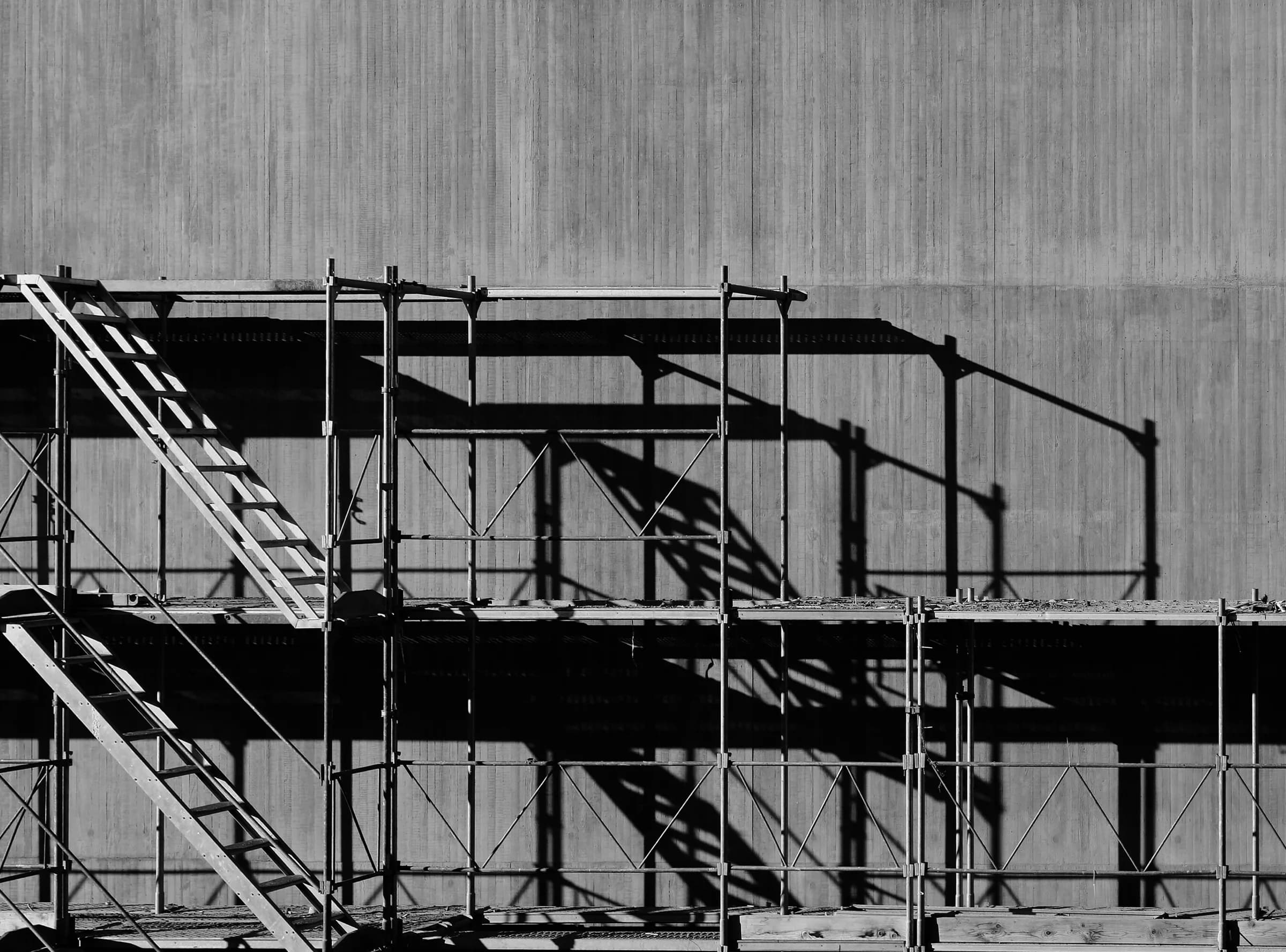 Beton bir yüzeyin önünde yükselen iskele ve merdiven düzeni, siyah beyaz