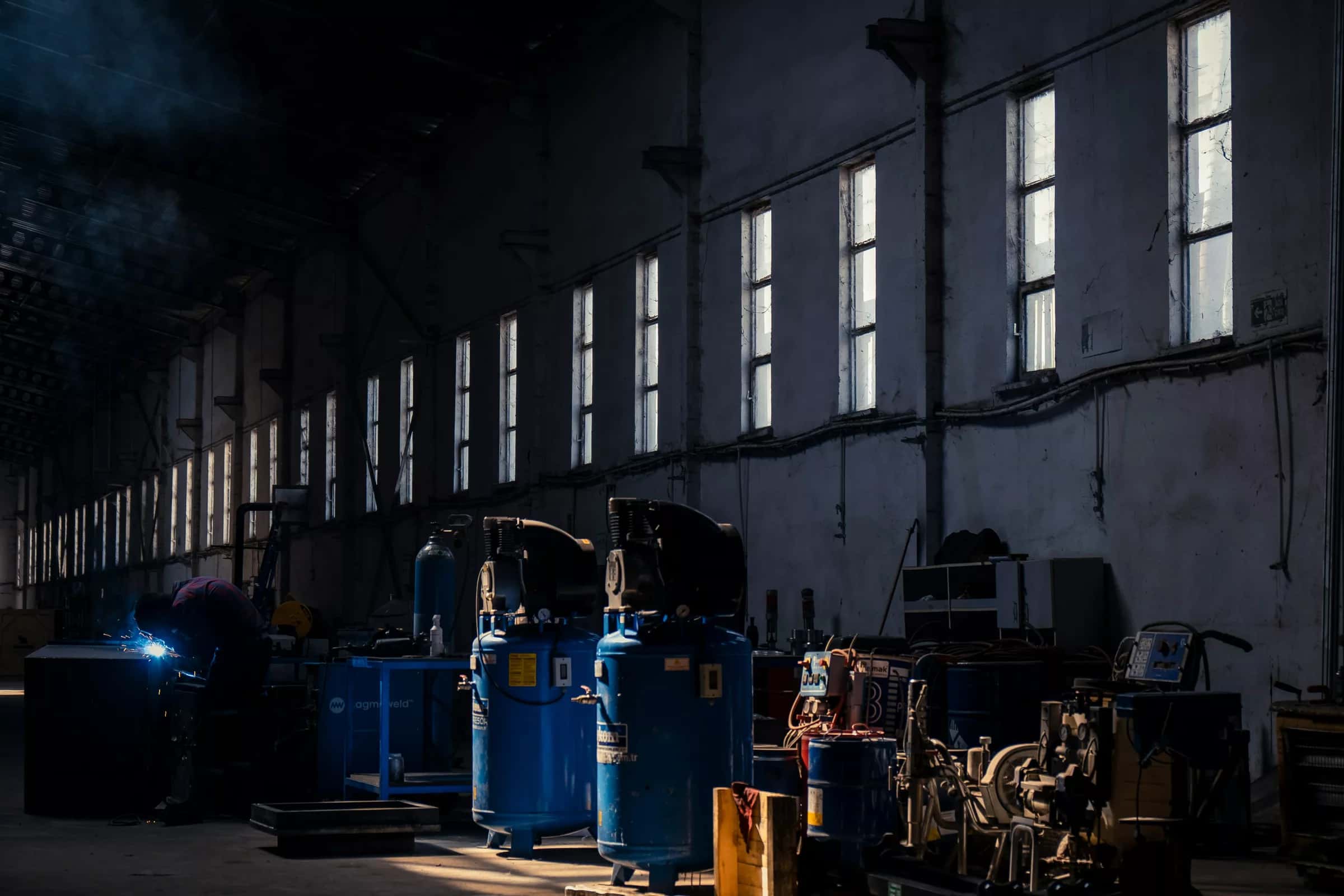 Yüksek tavanlı bir fabrika holü: sıra sıra pencerelerden düşen ışık, zeminde makineler