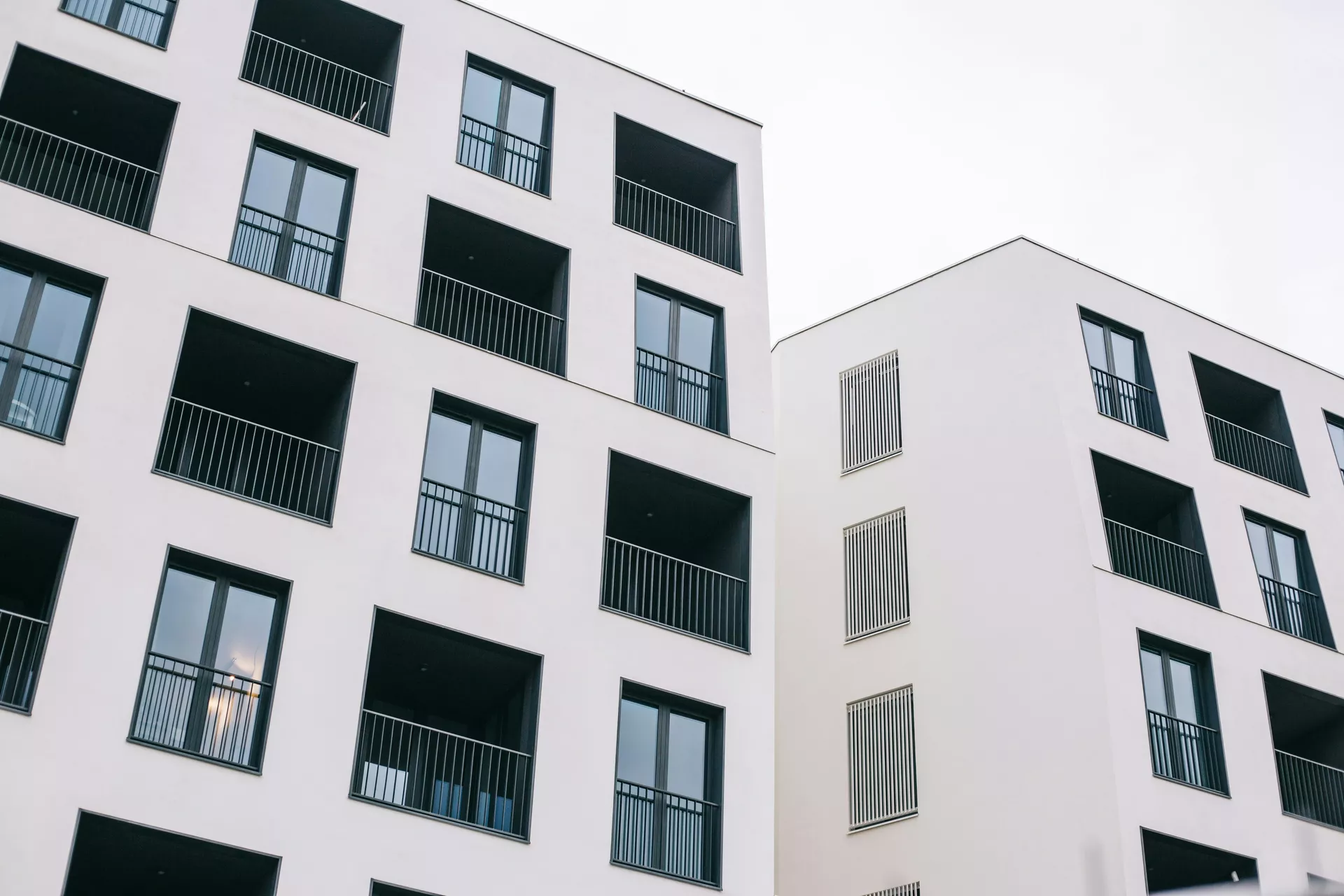Sarı sıvalı bir apartman cephesi, panjurlu pencereler ve saksılı balkonlar