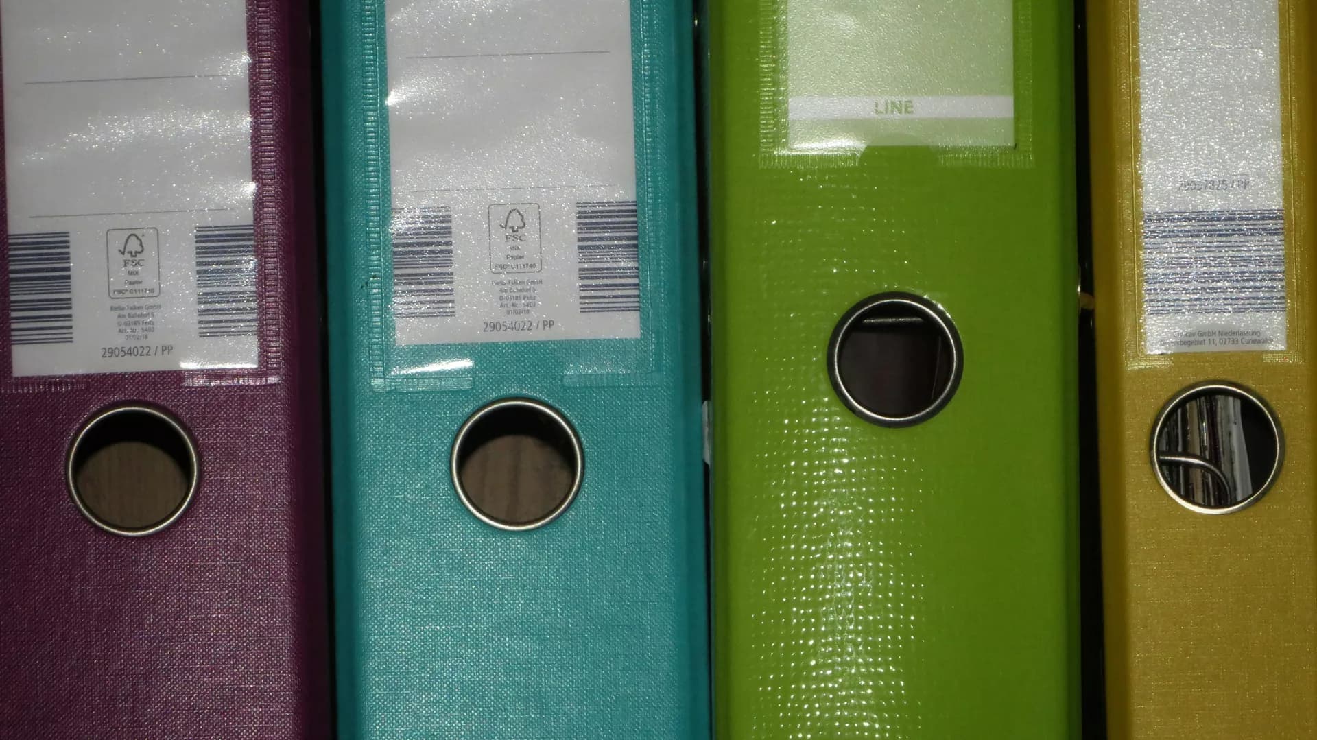 Bir ofis rafında yan yana dizilmiş, sırtları etiketli dosya klasörleri